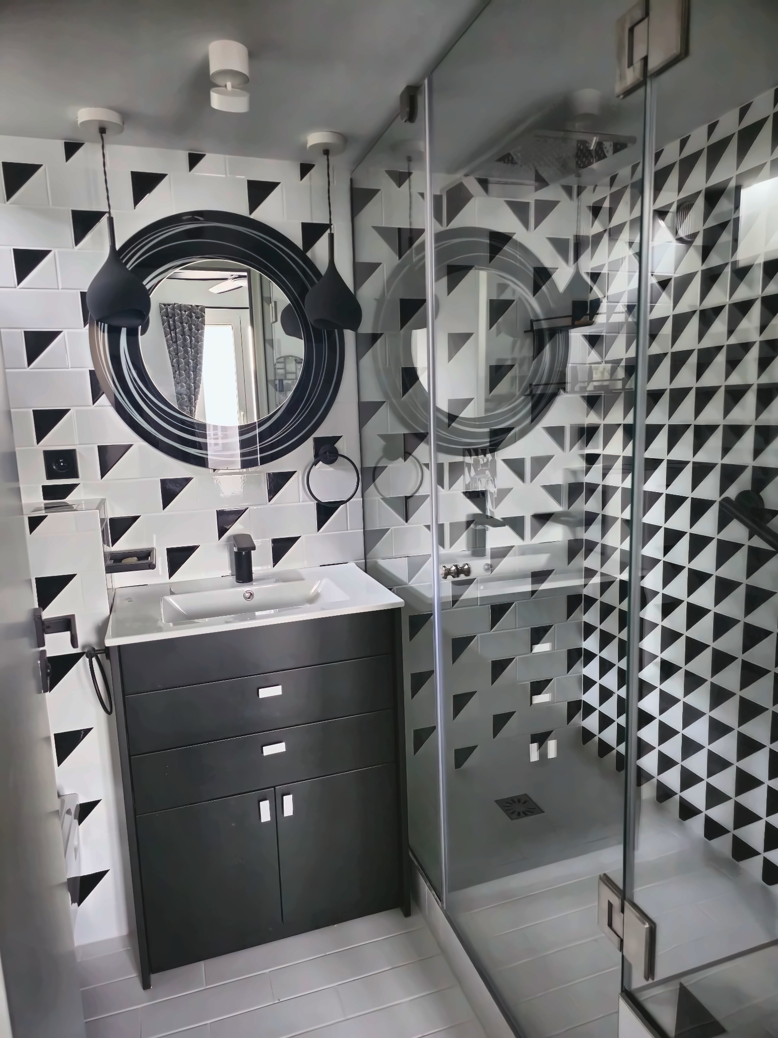Salle de bain graphique noir et blanc rénovée à Paris 15e avec meuble vasque noir et grand miroir rond