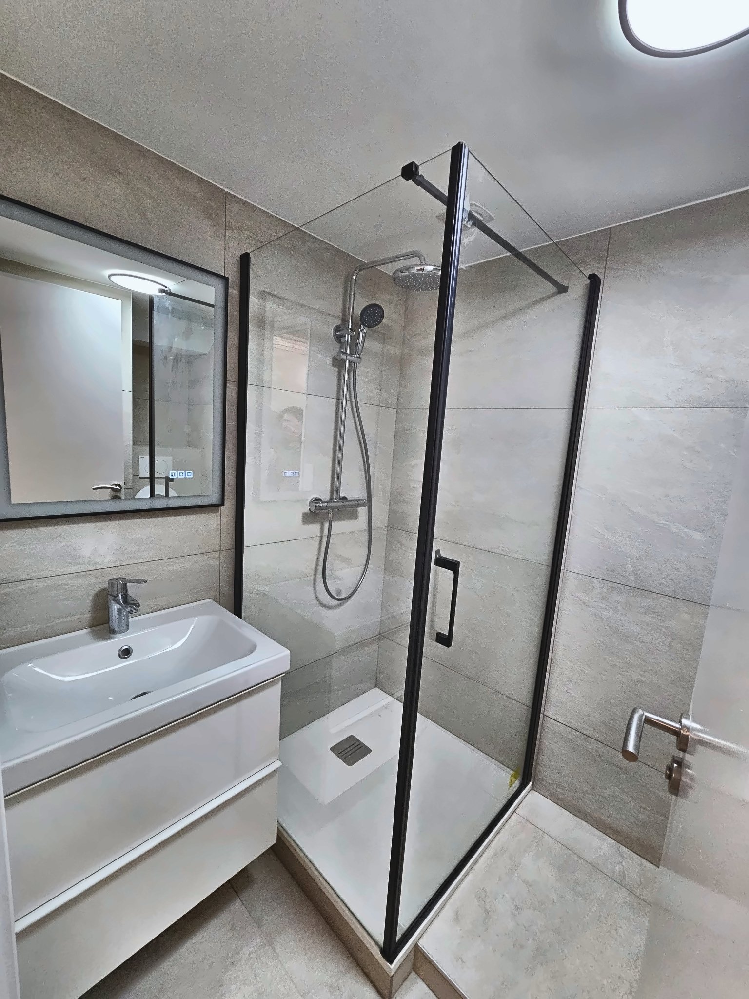 Salle de bain rénovée à Paris 15e — carrelage grand format gris, douche vitrée paroi noire, meuble blanc suspendu
