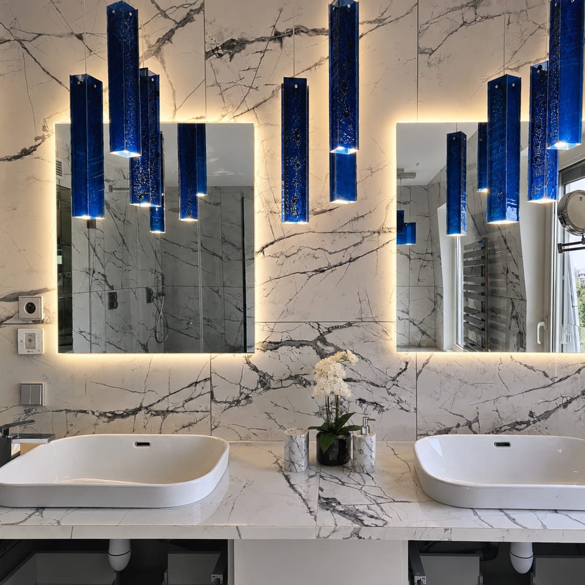 Salle de bain rénovée avec double vasque en marbre et suspensions en verre bleu à Paris 7e